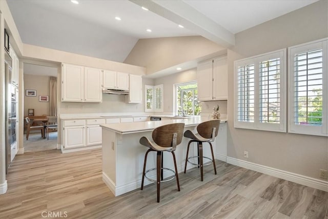 81 Via Larga Vis, Bonsall, CA 92003 - kitchen featuring under cabinet range hood, white cabinets, light countertops, light wood-type flooring, and lofted ceiling