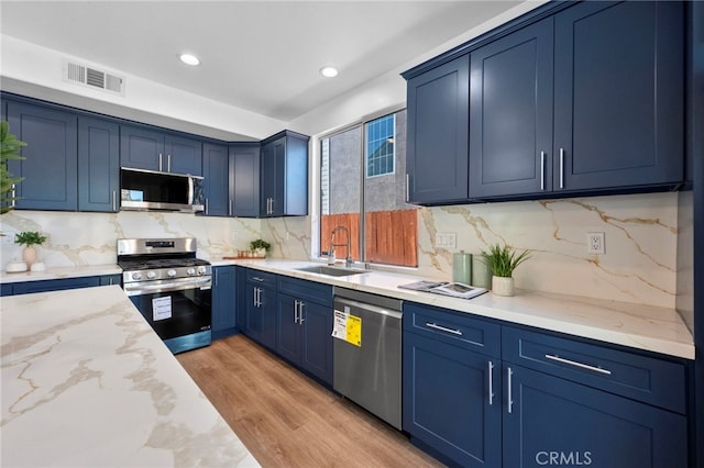 827 La Cadena Ln, Corona, CA 92879 - kitchen featuring stainless steel appliances, blue cabinetry, light stone counters, backsplash, and light wood finished floors