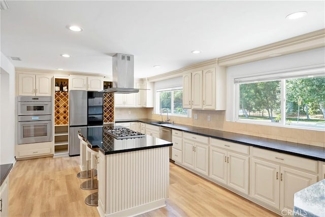 17211 Orozco St, Granada Hills, CA 91344 - kitchen featuring island range hood, dark countertops, light wood-style floors, stainless steel appliances, and backsplash