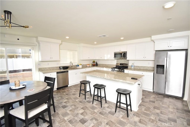 5280 Coyote St, Hemet, CA 92545 - kitchen featuring appliances with stainless steel finishes, white cabinets, a kitchen island, a kitchen bar, and stone finish floors