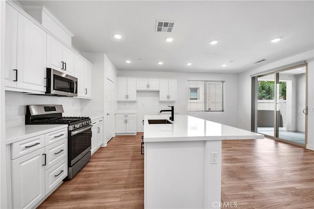 1660 Capri Way, Beaumont, CA 92223 - kitchen featuring appliances with stainless steel finishes, light wood-type flooring, a center island with sink, recessed lighting, and white cabinetry