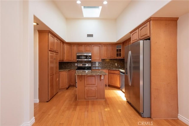 13341 Twin Hls Unit 57C, Seal Beach, CA 90740 - kitchen featuring stainless steel appliances, dark stone counters, light wood finished floors, a center island, and a high ceiling