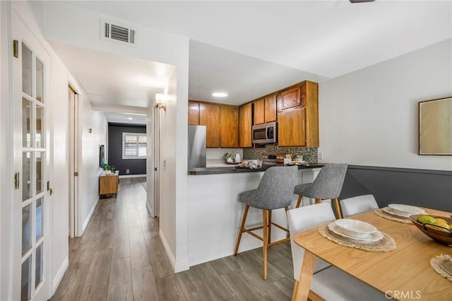 939 W Pine St Unit 44/D, Upland, CA 91786 - kitchen featuring brown cabinetry, wood finished floors, decorative backsplash, appliances with stainless steel finishes, and dark countertops