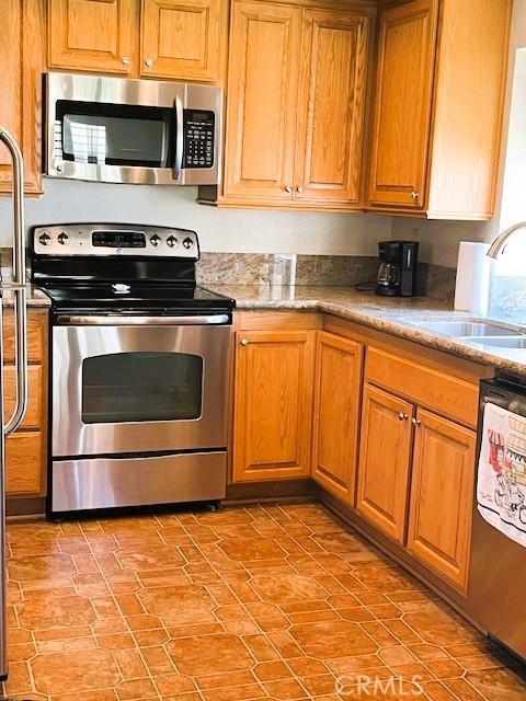 13212 La Jolla Cir Unit 307B, La Mirada, CA 90638 - kitchen with stainless steel appliances, brown cabinetry, and light stone countertops