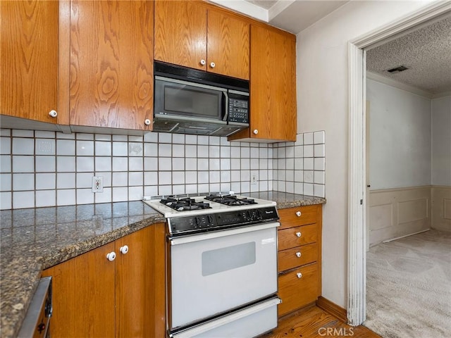10348 Woodbridge St, Toluca Lake, CA 91602 - kitchen with brown cabinetry, white gas stove, a textured ceiling, black microwave, and wainscoting