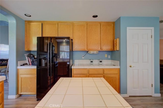 1166 Labrador Ct, Newman, CA 95360 - kitchen with tile countertops, wood finished floors, arched walkways, and black refrigerator with ice dispenser