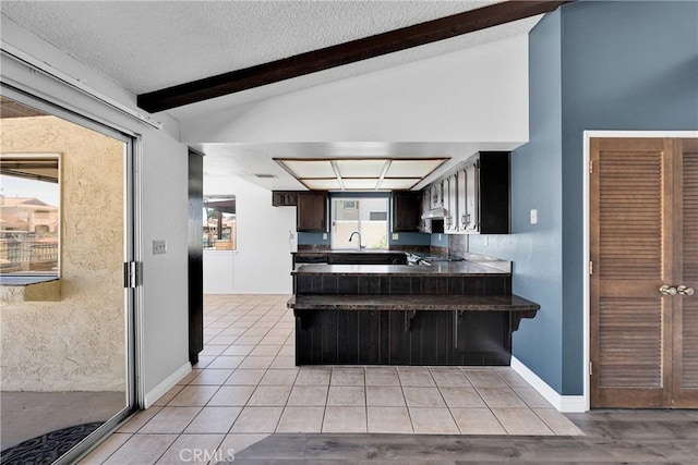 26453 Buccaneer Ln, Helendale, CA 92342 - kitchen featuring dark countertops, a peninsula, light tile patterned floors, a textured ceiling, and a breakfast bar area