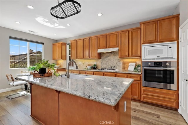 7 Sachem Way, Ladera Ranch, CA 92694 - kitchen with stainless steel oven, brown cabinets, light wood-style floors, light stone counters, and tasteful backsplash