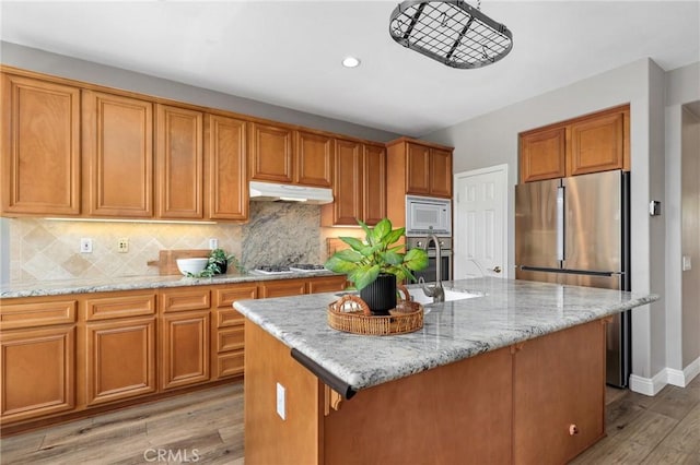 7 Sachem Way, Ladera Ranch, CA 92694 - kitchen featuring appliances with stainless steel finishes, light wood-style floors, brown cabinets, light stone counters, and decorative backsplash