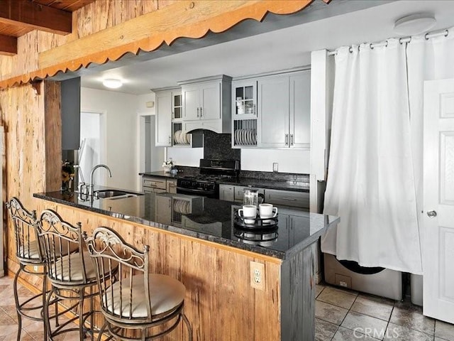 20319 Vanowen St, Winnetka, CA 91306 - kitchen featuring light tile patterned floors, a kitchen breakfast bar, black range with gas cooktop, glass insert cabinets, and dark stone counters