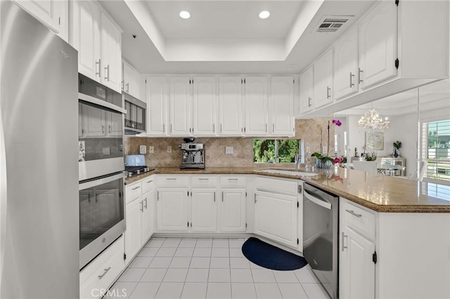 5224 Zelzah Ave Unit 208, Encino, CA 91316 - kitchen with appliances with stainless steel finishes, a peninsula, light tile patterned floors, a tray ceiling, and tasteful backsplash