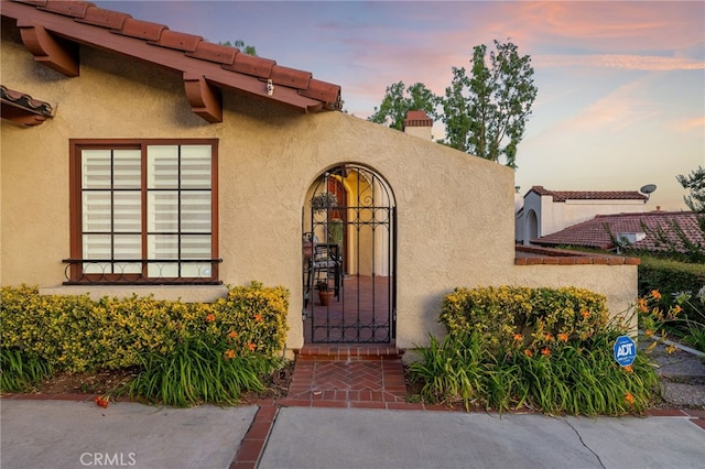 1610 Via Estrella, Pomona, CA 91768 - exterior entry at dusk with stucco siding, a gate, and a chimney