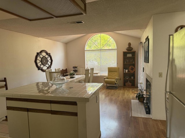 1826 Via Cuarto, Oceanside, CA 92056 - kitchen with tile countertops, vaulted ceiling, freestanding refrigerator, light wood-style flooring, and a fireplace with flush hearth