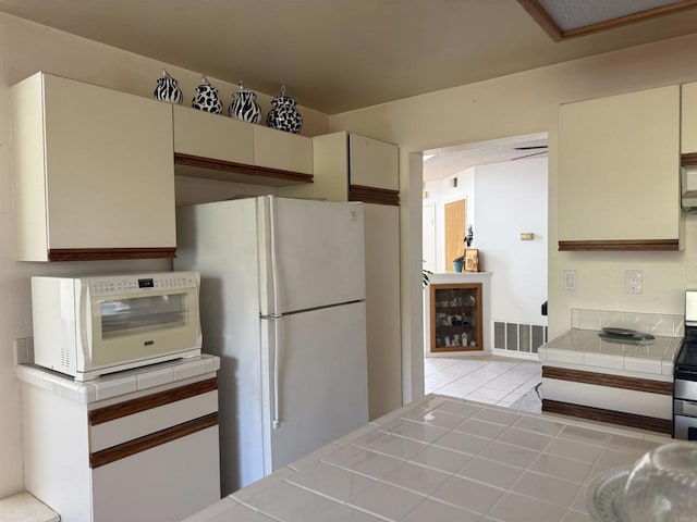 1826 Via Cuarto, Oceanside, CA 92056 - kitchen featuring tile counters, freestanding refrigerator, cream cabinetry, light tile patterned floors, and stainless steel range