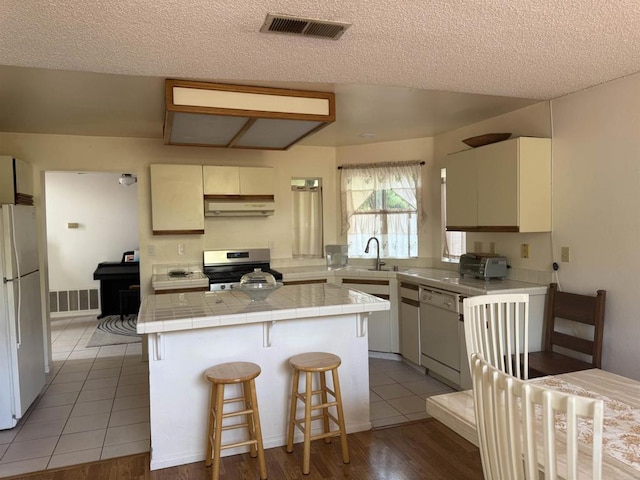 1826 Via Cuarto, Oceanside, CA 92056 - kitchen with white appliances, a center island, a textured ceiling, a kitchen breakfast bar, and tile counters
