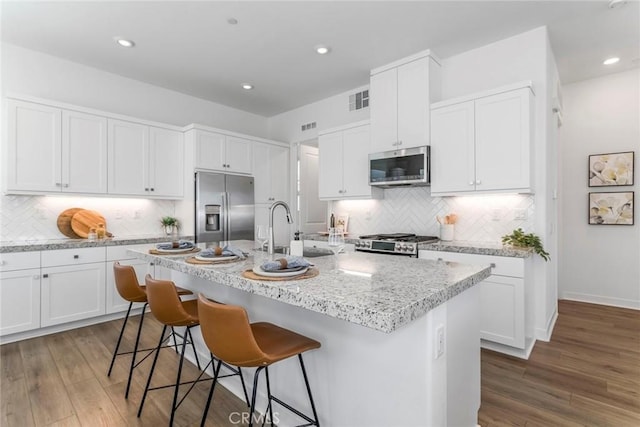27554 Sparrow Ct, Valencia, CA 91381 - kitchen with appliances with stainless steel finishes, wood finished floors, a kitchen island with sink, decorative backsplash, and recessed lighting