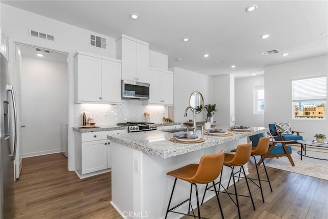 27554 Sparrow Ct, Valencia, CA 91381 - kitchen with dark wood finished floors, a breakfast bar, a center island with sink, recessed lighting, and backsplash