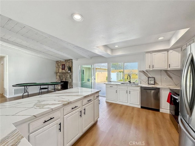 1472 N San Antonio Ave, Upland, CA 91786 - kitchen featuring a stone fireplace, stainless steel appliances, light wood-type flooring, white cabinets, and light stone countertops