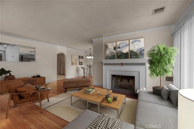404 W Robinson Ave, Fresno, CA 93705 - living room featuring arched walkways, wood finished floors, ornamental molding, a brick fireplace, and a chandelier