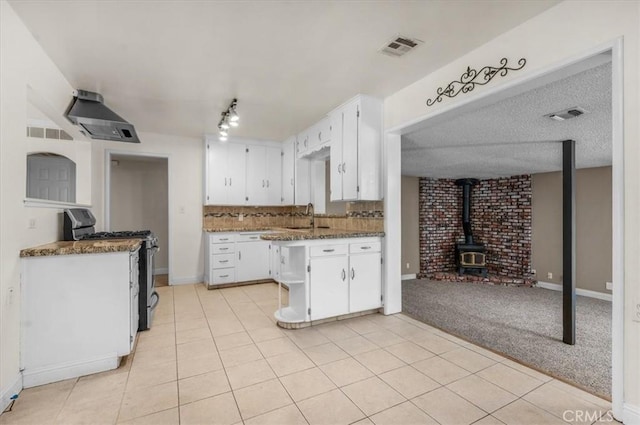 404 W Robinson Ave, Fresno, CA 93705 - kitchen with gas stove, a wood stove, white cabinets, and wall chimney range hood