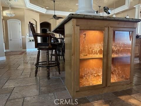17134 Joshua Rd, Apple Valley, CA 92307 - bar featuring stone tile flooring, a ceiling fan, arched walkways, ornamental molding, and a raised ceiling