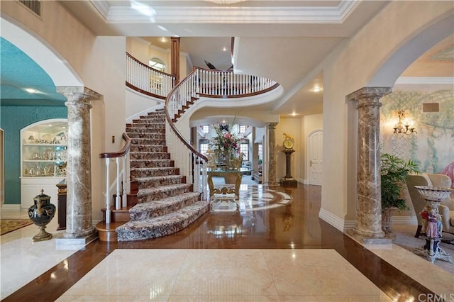 tiled entryway featuring a notable chandelier, a towering ceiling, crown molding, and decorative columns