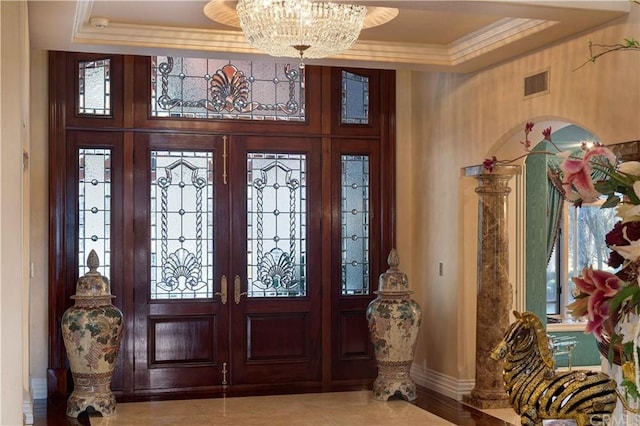 foyer entrance with a notable chandelier, light tile floors, a raised ceiling, crown molding, and french doors