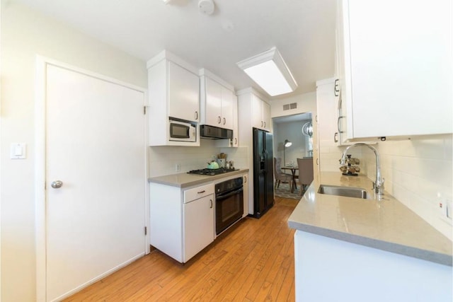 kitchen featuring white cabinets, exhaust hood, light wood-type flooring, black appliances, and sink