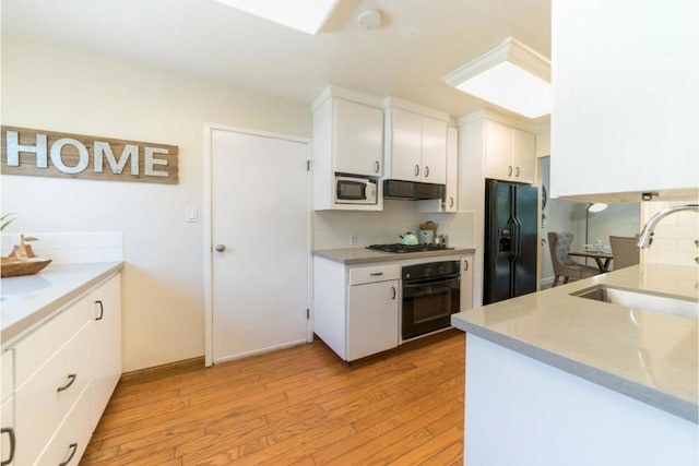 kitchen with white cabinets, sink, light hardwood / wood-style flooring, backsplash, and black appliances