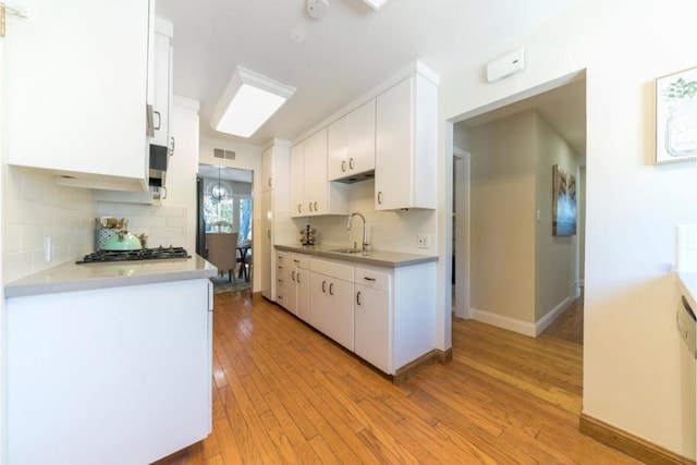 kitchen with stainless steel gas stovetop, white cabinets, light hardwood / wood-style floors, and sink