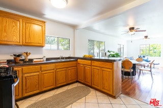 kitchen with black range oven, light tile patterned flooring, kitchen peninsula, ceiling fan, and sink