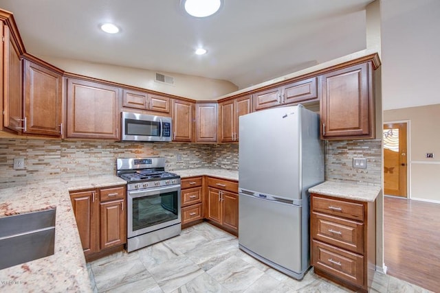 kitchen with light wood-type flooring, lofted ceiling, stainless steel appliances, light stone countertops, and backsplash