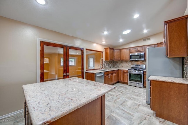 kitchen featuring lofted ceiling, light tile patterned floors, decorative backsplash, appliances with stainless steel finishes, and light stone countertops