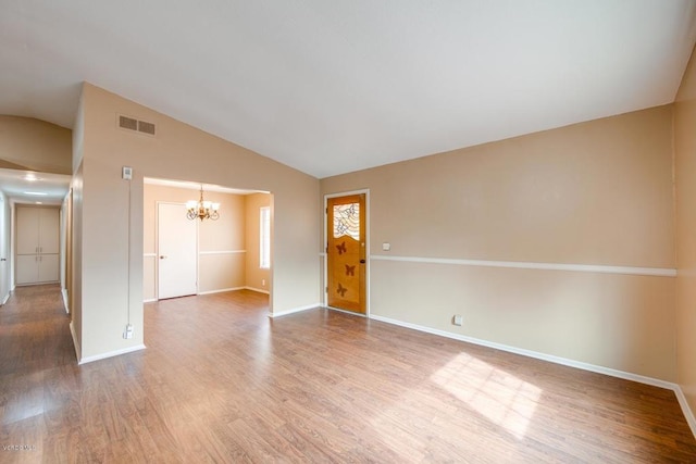 spare room featuring high vaulted ceiling, an inviting chandelier, and hardwood / wood-style flooring