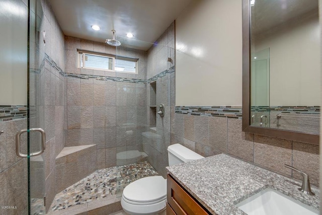 bathroom with tile walls, walk in shower, vanity, and toilet