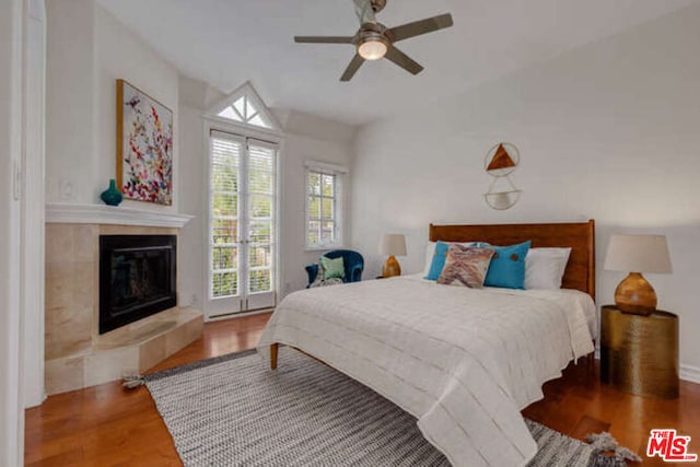 bedroom featuring ceiling fan, a tile fireplace, and hardwood / wood-style flooring