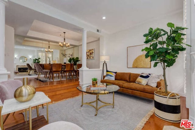 living room featuring decorative columns, hardwood / wood-style flooring, a raised ceiling, and an inviting chandelier