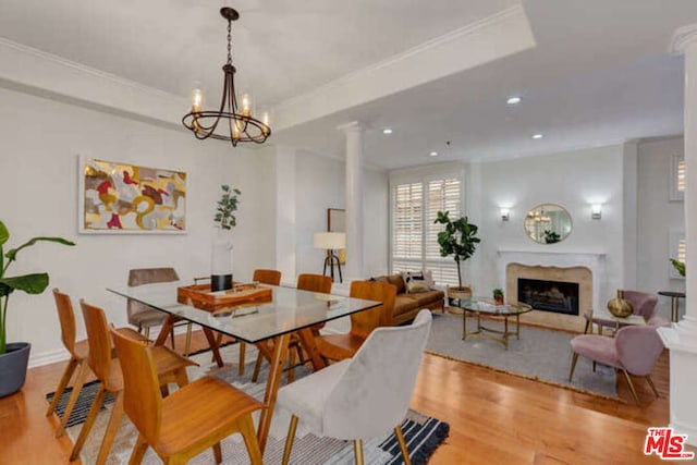 dining area with a raised ceiling, a chandelier, ornate columns, a fireplace, and light wood-type flooring