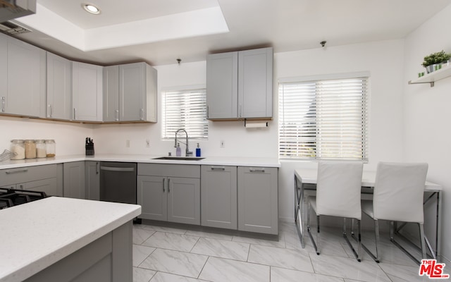 kitchen with light tile patterned floors, sink, a tray ceiling, stainless steel dishwasher, and gray cabinetry