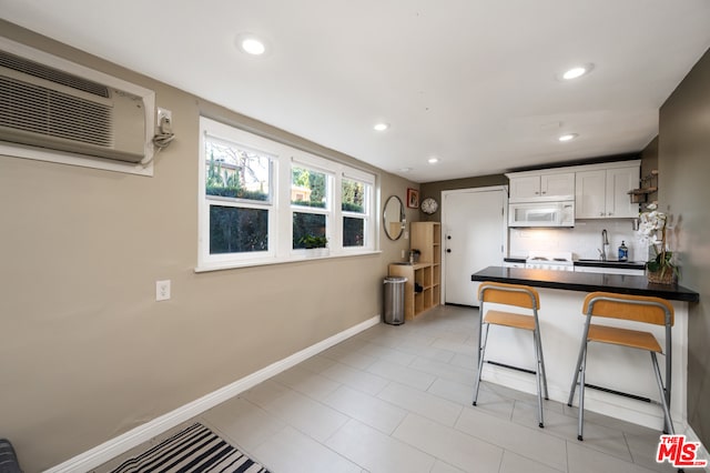 kitchen with a kitchen bar, tasteful backsplash, light tile floors, and white cabinetry