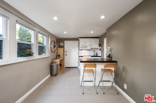 kitchen featuring kitchen peninsula, sink, a kitchen breakfast bar, white cabinets, and light tile flooring