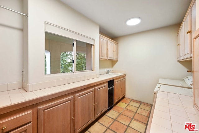 kitchen featuring sink, light tile patterned flooring, independent washer and dryer, and tile countertops