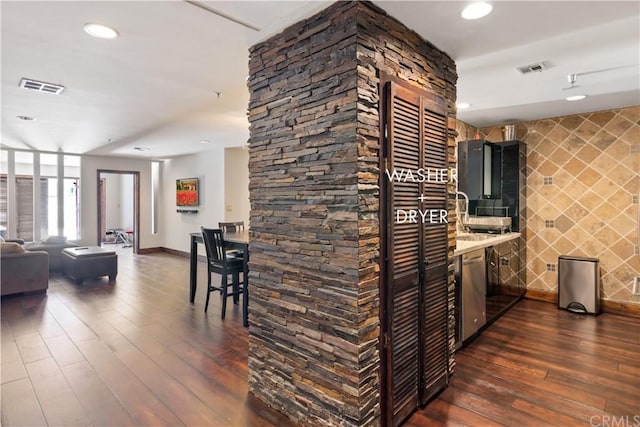 kitchen featuring dark hardwood / wood-style floors, stainless steel dishwasher, tile walls, and light stone counters