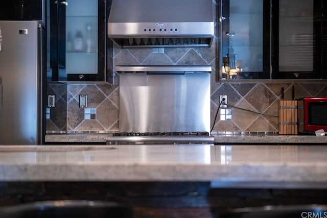 kitchen featuring stainless steel fridge, decorative backsplash, and wall chimney range hood