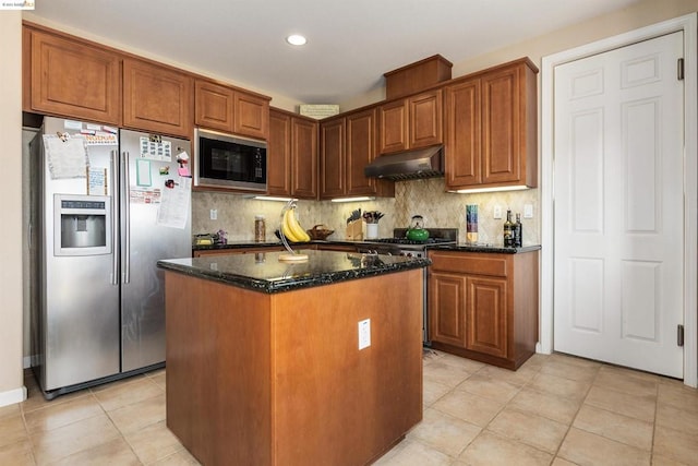 kitchen with light tile floors, dark stone counters, a kitchen island, appliances with stainless steel finishes, and backsplash