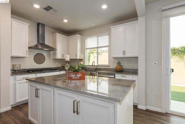 kitchen featuring wall chimney range hood, a kitchen island, and white cabinets