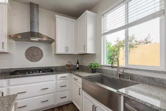 kitchen featuring wall chimney range hood, dark stone counters, appliances with stainless steel finishes, white cabinets, and dark hardwood / wood-style floors