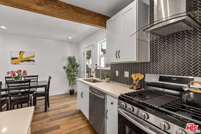 kitchen with wall chimney exhaust hood, appliances with stainless steel finishes, white cabinets, light wood-type flooring, and sink