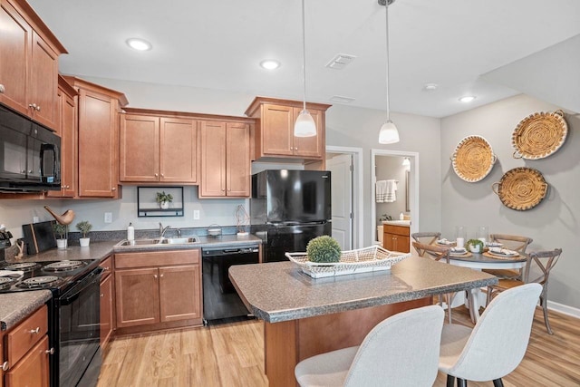 kitchen with sink, black appliances, light hardwood / wood-style flooring, a kitchen island, and pendant lighting