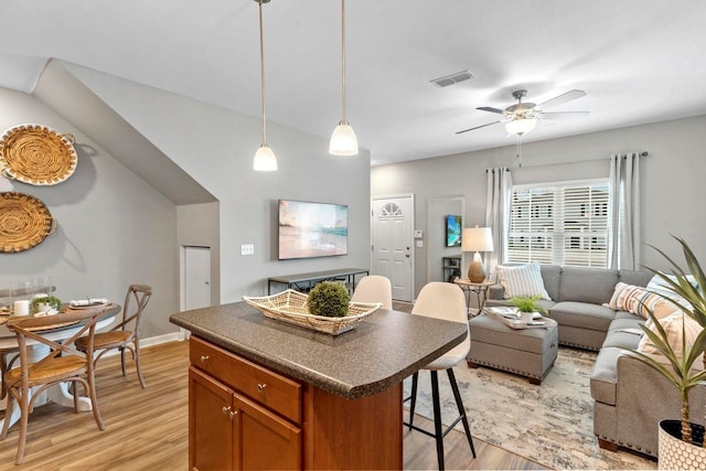 kitchen featuring a kitchen breakfast bar, ceiling fan, decorative light fixtures, light hardwood / wood-style flooring, and a center island